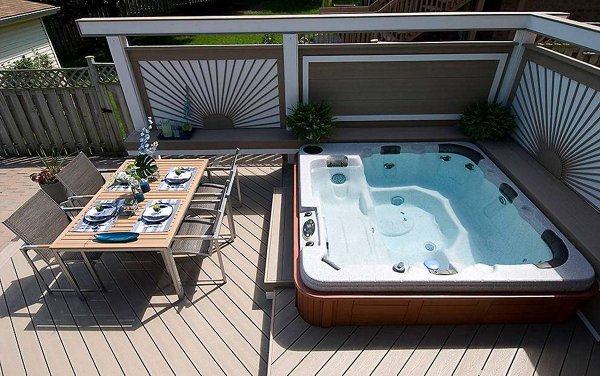 Hot tub built into a grey composite deck with glass railings in the background