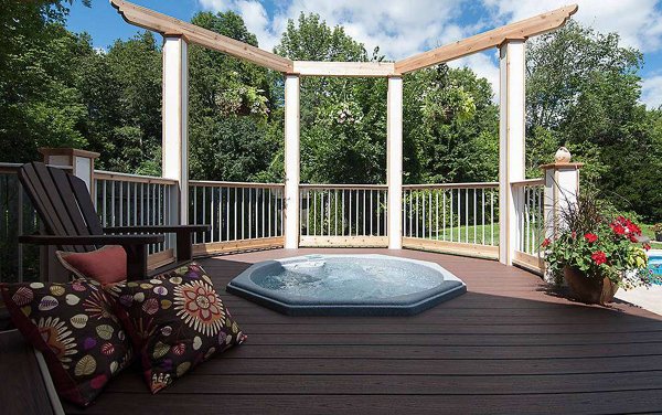 Hot tub built into a grey composite deck with glass railings in the background
