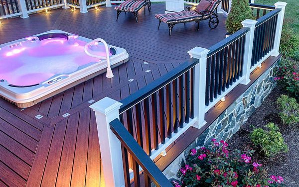Hot tub built into a grey composite deck with glass railings in the background