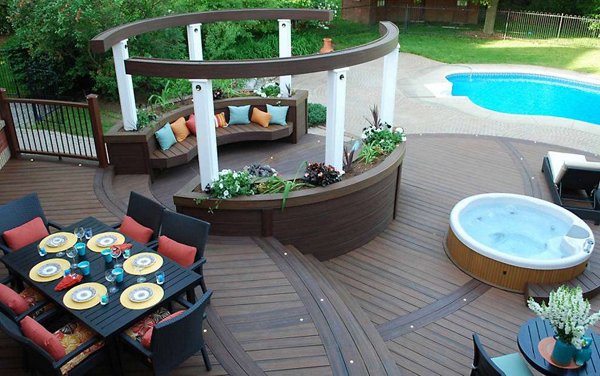 Hot tub built into a grey composite deck with glass railings in the background