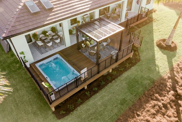 Hot tub built into a grey composite deck with glass railings in the background