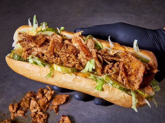 Black glove hand holding chicken po boy with lettuce and pickles 