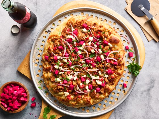 Chicken Shawarma Pizza on a cutting board with a drink and pizza cutter beside it.