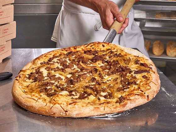 Steak and onion pizza being station on a metal table by a chef with a peel