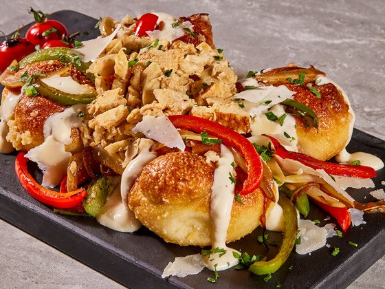 Garlic knot bread topped with chicken, red and green bell peppers and cheese sauce