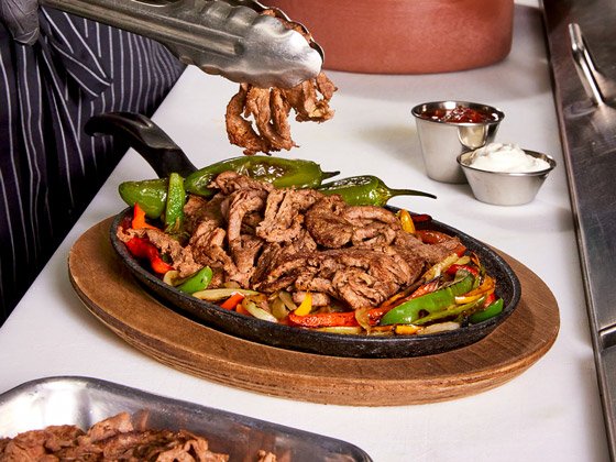 Cast iron plated steak fajitas with bell peppers, onions and sauces on the side