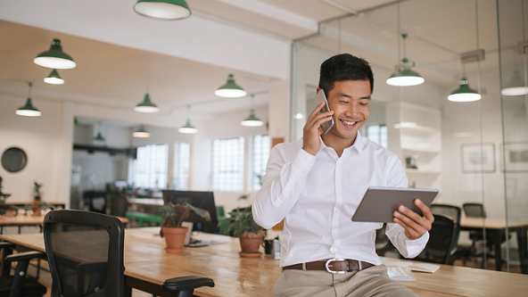 Male looking at a tablet while talking on his smart phone in an office 
