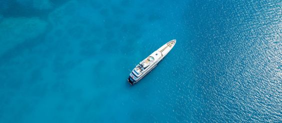 An overhead view of a large private yacht in a bright blue sea.