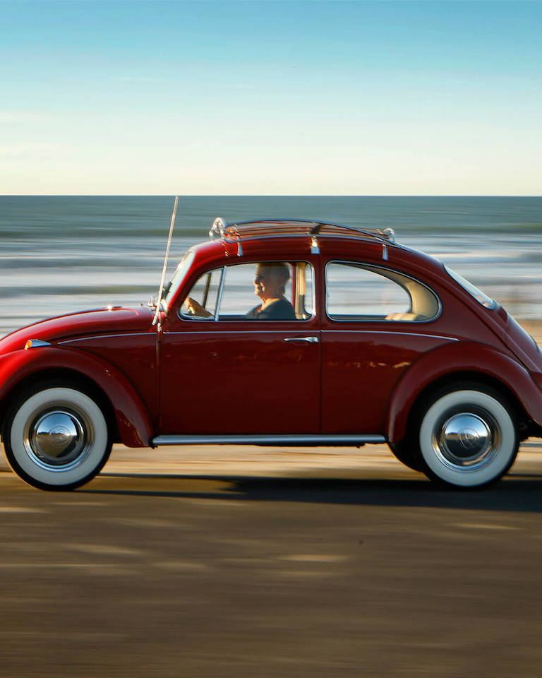 Kathleen Brooks drives her restored 1967 Volkswagen Beetle by the ocean.