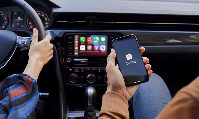 The hand of a person sitting in the front passenger seat of a VW holds their iPhone as it’s connected to App-Connect