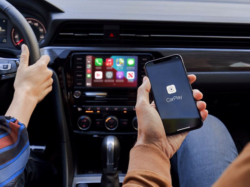 The hand of a person sitting in the front passenger seat of a VW holds their iPhone as it’s connected to App-Connect