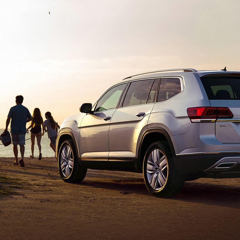 Volkswagen Atlas parked facing the beach with a group of people walking toward the beach. 