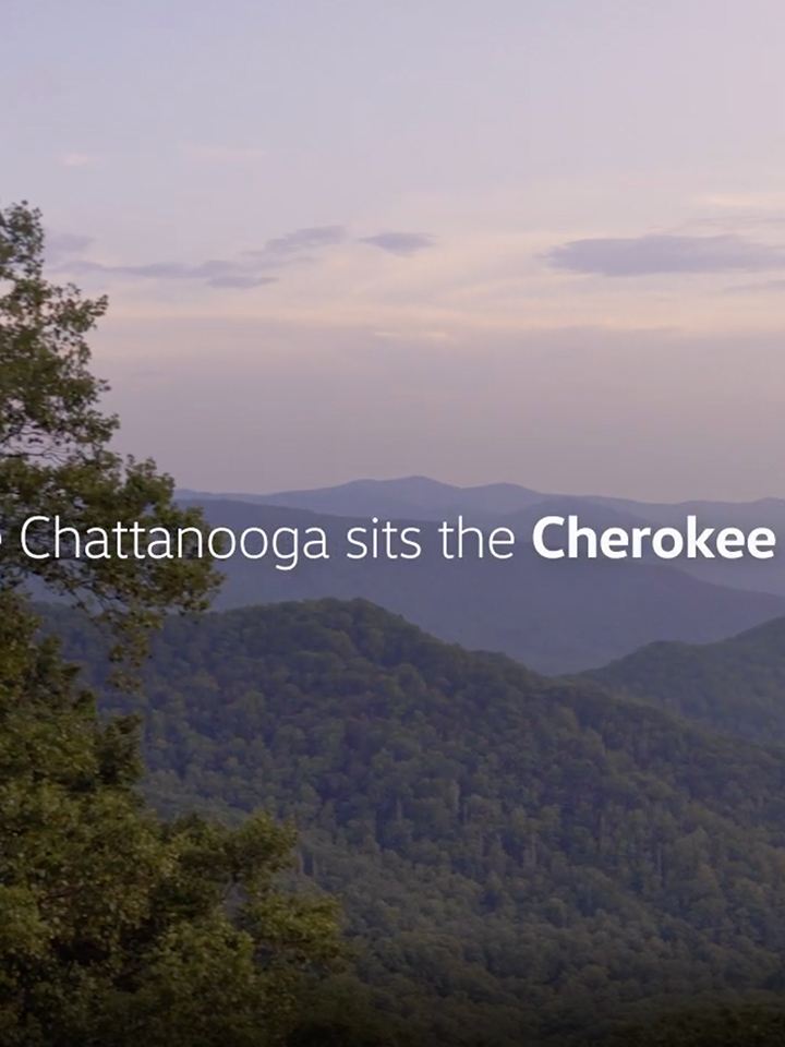 Un cielo azul lavanda con montañas boscosas y un texto que dice A una hora de Chattanooga se encuentra el Bosque Nacional Cherokee.