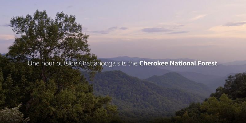 Un cielo azul lavanda con montañas boscosas y un texto que dice A una hora de Chattanooga se encuentra el Bosque Nacional Cherokee.