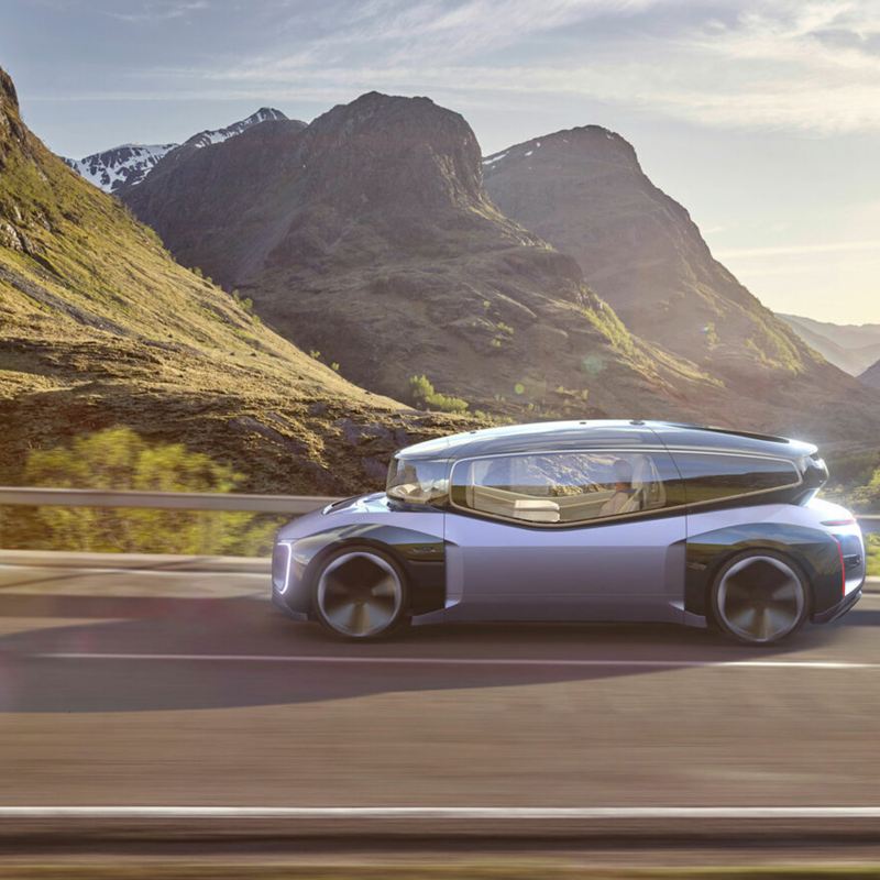A futuristic looking concept car called the GEN.TRAVEL with a distinct design divided into two parts: the top features a transparent, glass cabin and the body, a metallic purple. The car drives down a scenic mountain highway. 