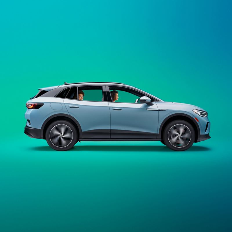 A profile shot of a woman driving an ID.4 shown in Arctic Blue Metallic on a green gradient background. A child sits in the backseat looking out the passenger side window. Wheels are blurred to simulate forward motion.