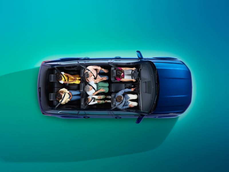 A cutaway perspective view from above, looking directly down into the interior of an Atlas shows the vehicle’s ample room to fit up to seven. Behind the driver and front passenger, three passengers sit in the second row, and two in the third row. The Atlas shown in Tourmaline Blue Metallic is parked on a colorful teal gradient background. 