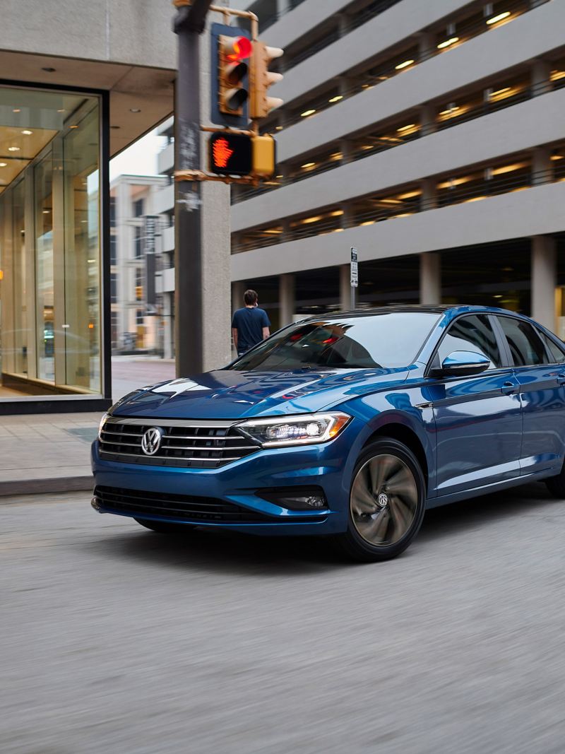 Toma de un Passat R-Line de Volkswagen color Tourmaline Blue Metallic virando a la derecha en el corazón de una calle céntrica.