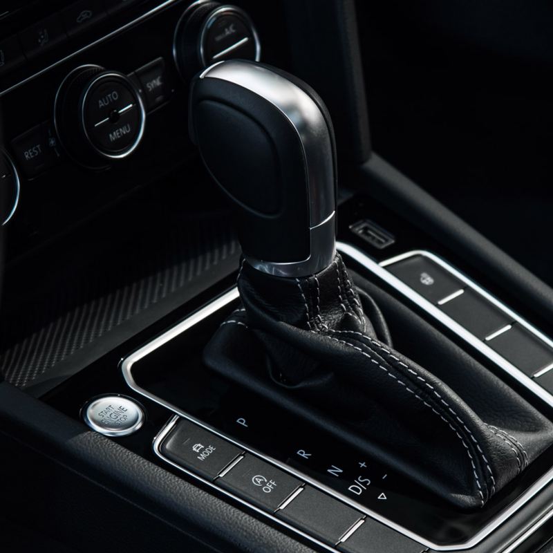 Keyless push-start button and brushed silver trim accompany stitched black leather gear shift of Volkswagen vehicle.