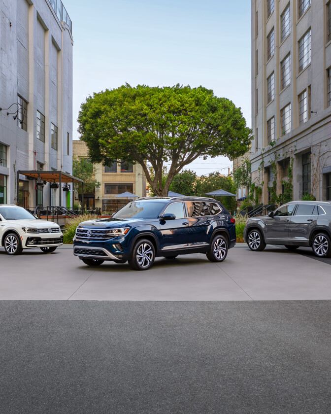 Atlas in Tourmaline Blue Metallic, an Atlas Cross Sport in Pure Gray, and a Tiguan in Pure White are parked on an urban street.