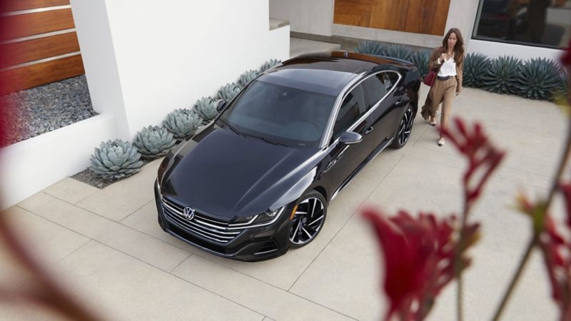 In a residential driveway, a woman walks toward the driver’s side of a parked Arteon in Deep Black Pearl.