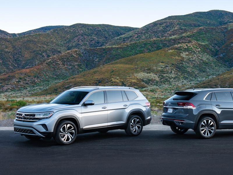 The 2021.5 Atlas and 2020 Atlas Cross Sport parked in front of mountains, showing front 3/4 and rear 3/4 views respectively.