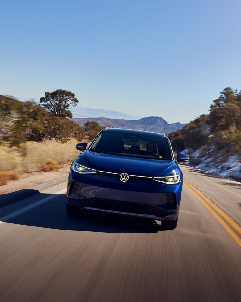 Front-end view of a 2021 Volkswagen ID.4 driving down a two-lane highway with mountains in the background. 