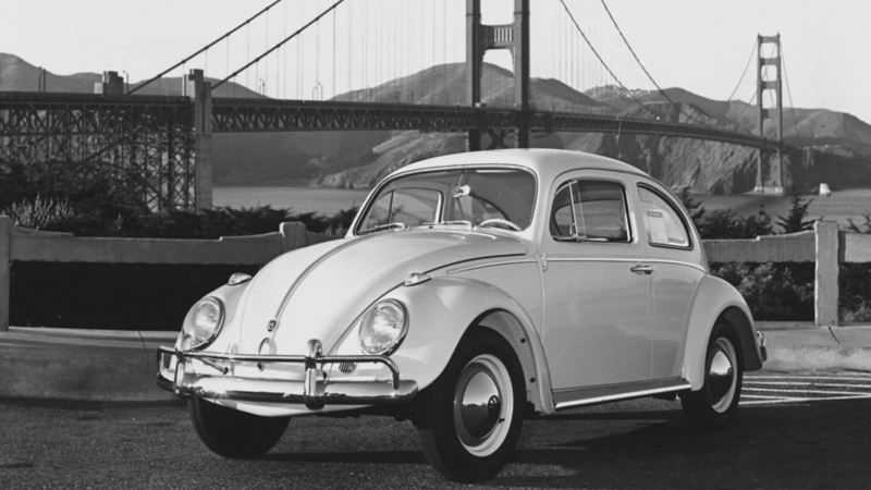 A vintage Volkswagen Beetle sits in front of the Golden Gate Bridge.