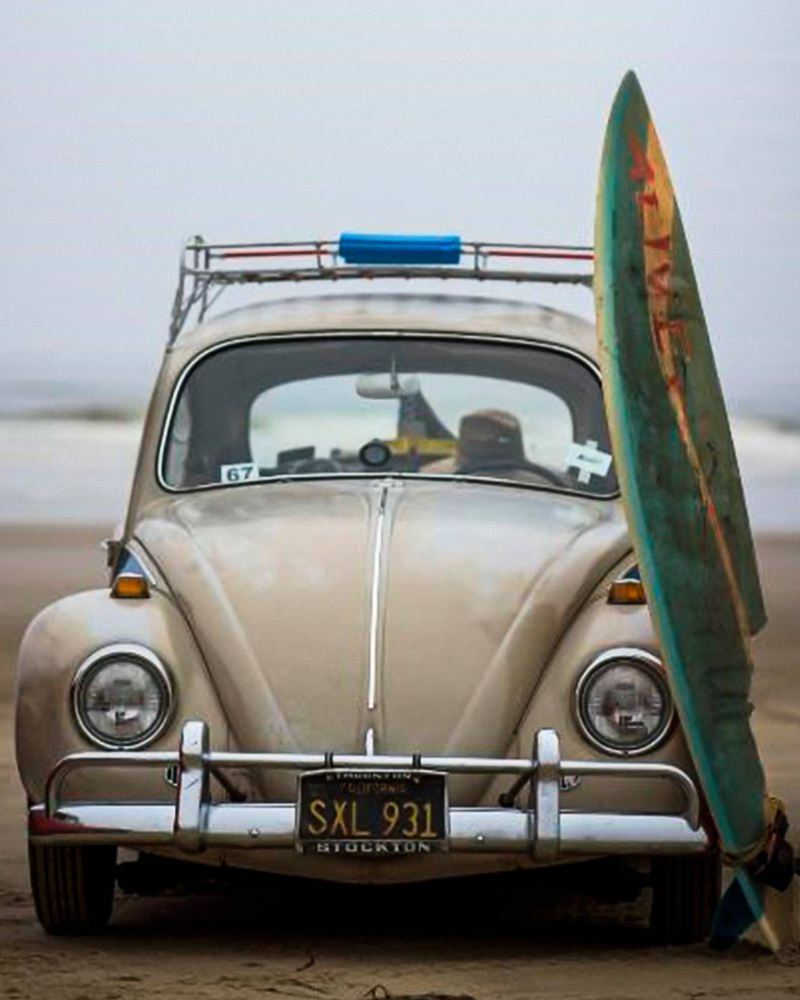 Vintage Volkswagen Beetle parked by the beach with a surfboard