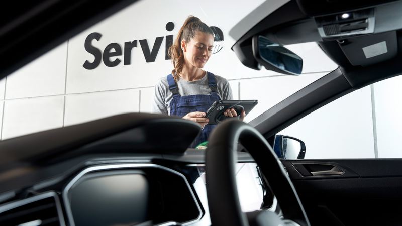A woman looks at her tablet device in front of a VW parked at a service center.
