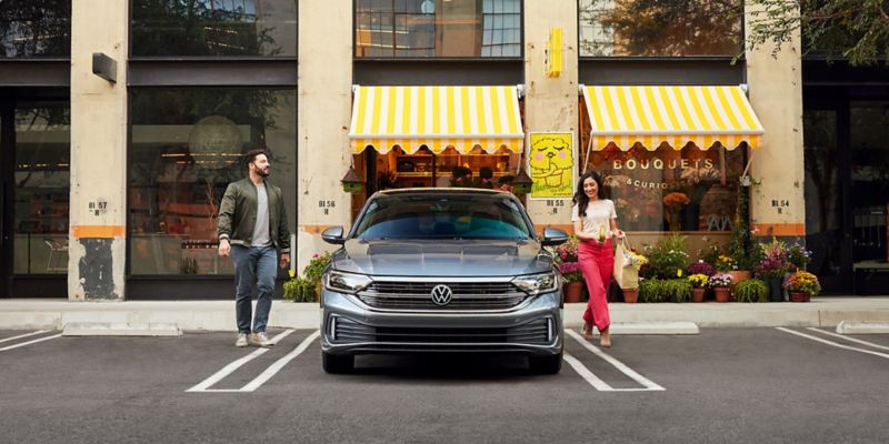 Two people walk toward a Jetta shown in Platinum Gray Metallic parked in front of a flower store.