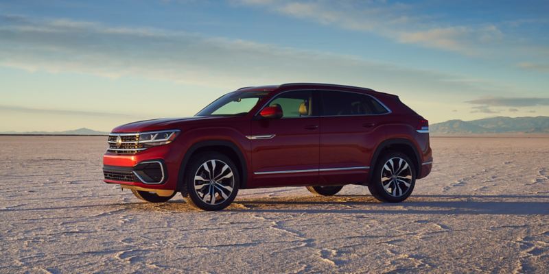The Atlas Cross Sport in Aurora Red  Metallic as seen from the side parked alongside a mountain and lake.