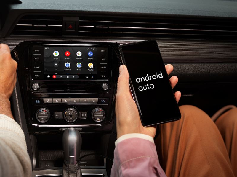 The hand of a person sitting in the front passenger seat holding their Android phone as it’s connected to App-Connect.