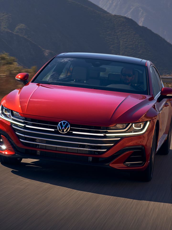 Front view of the Arteon in Kings Red Metallic driving on two-lane highway with mountains in background.