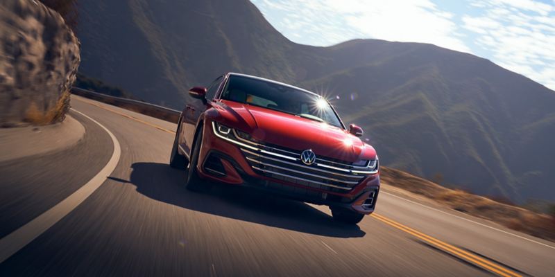 A front view of an Arteon shown in Kings Red Metallic, driving on a two-lane road with mountains behind it. 
