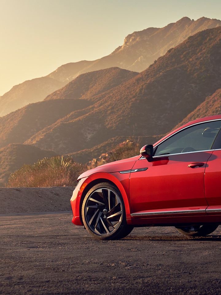 A profile shot of an Arteon shown in Kings Red Metallic, parked along a scenic overlook with foothills in the background. 