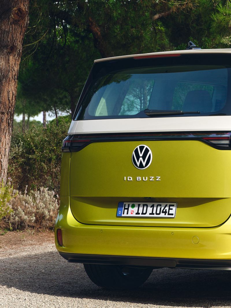 A ¾ rear shot of an ID. Buzz in Candy White and Lime Yellow parked in a driveway, featuring a wall mounted home charging port.