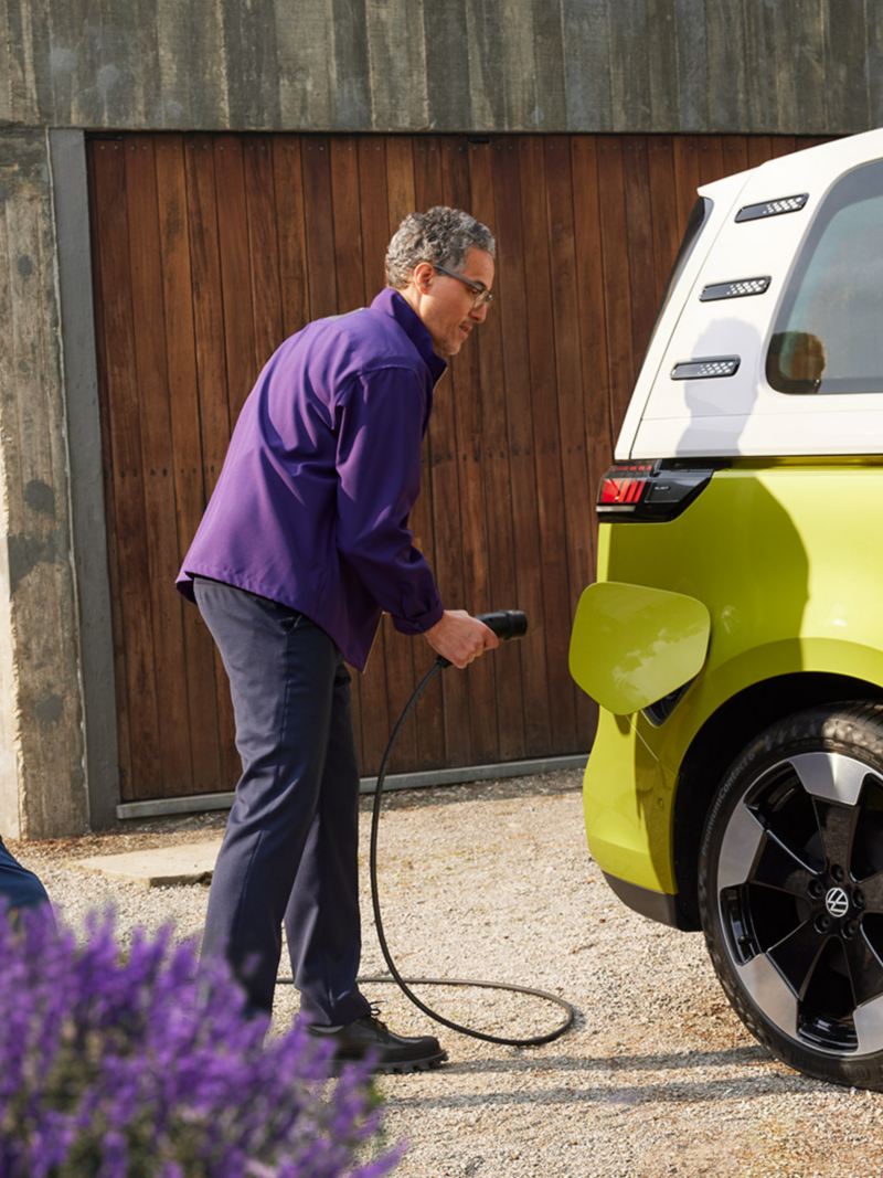A man in his driveway plugs a charging chord into a Candy White and Lime Yellow ID. Buzz.