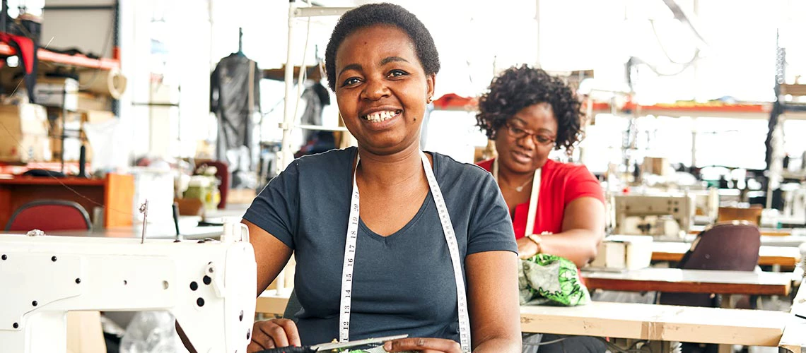 Two Zimbabwean women working in a textile factory on the sewing line using sewing machines, measuring tapes and scissors to stitch lining in African styled patterned fabric garment