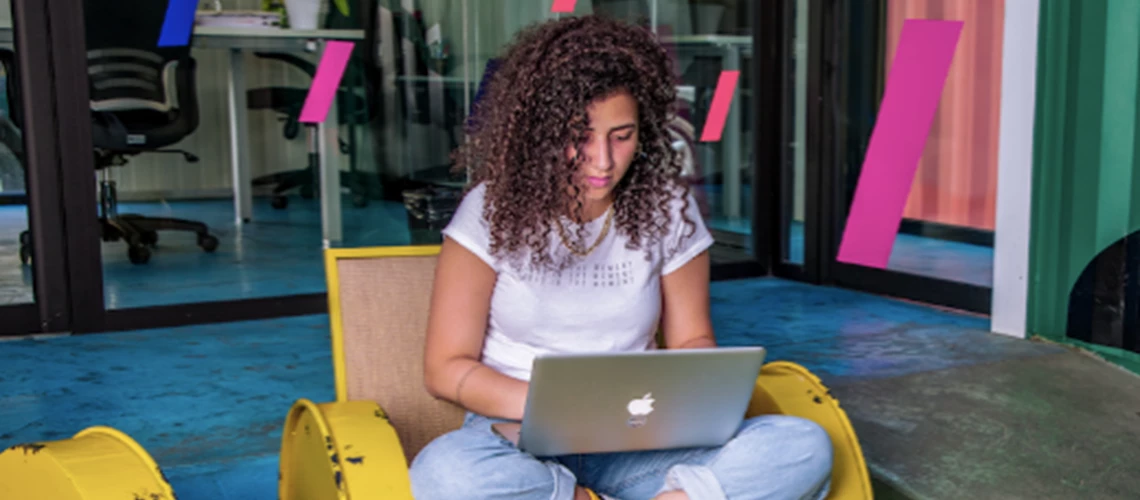 A young person types on their computer while sat in a chair.