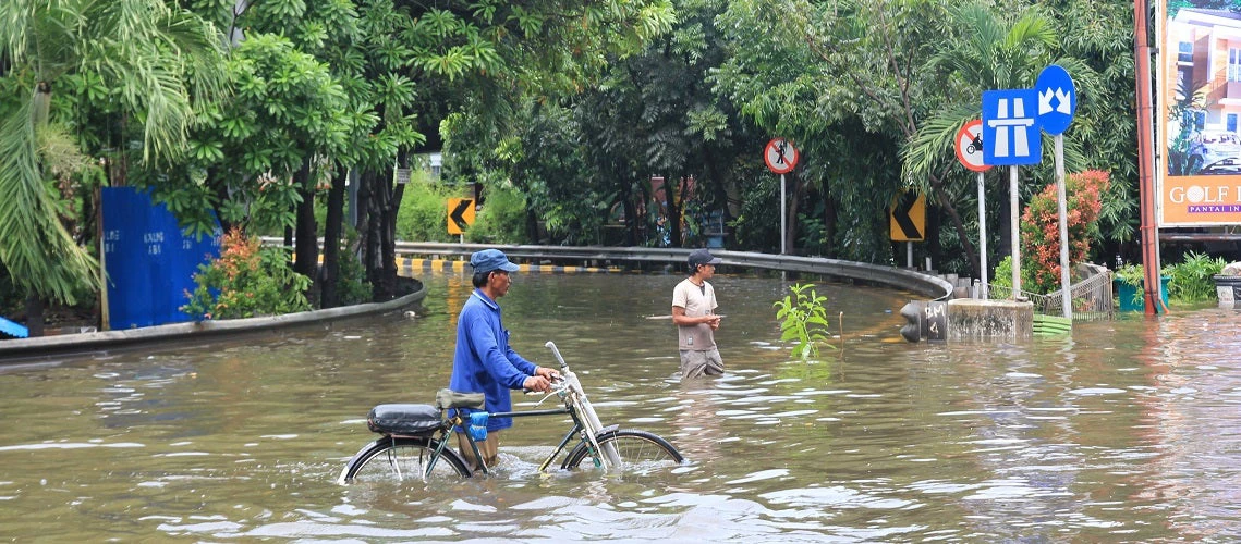 Man with a bicycle crossing a flooded road, waist deep in water, in Indonesia. 