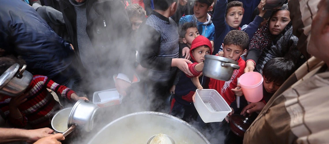 People and children stand around a cauldron of food in the West Bank.