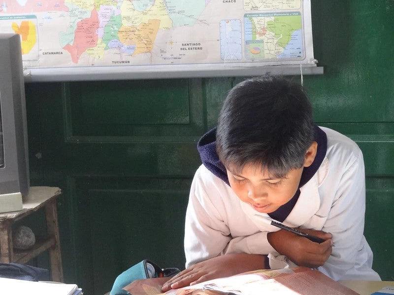 Niño leyendo en la escuela con un mapa detrás