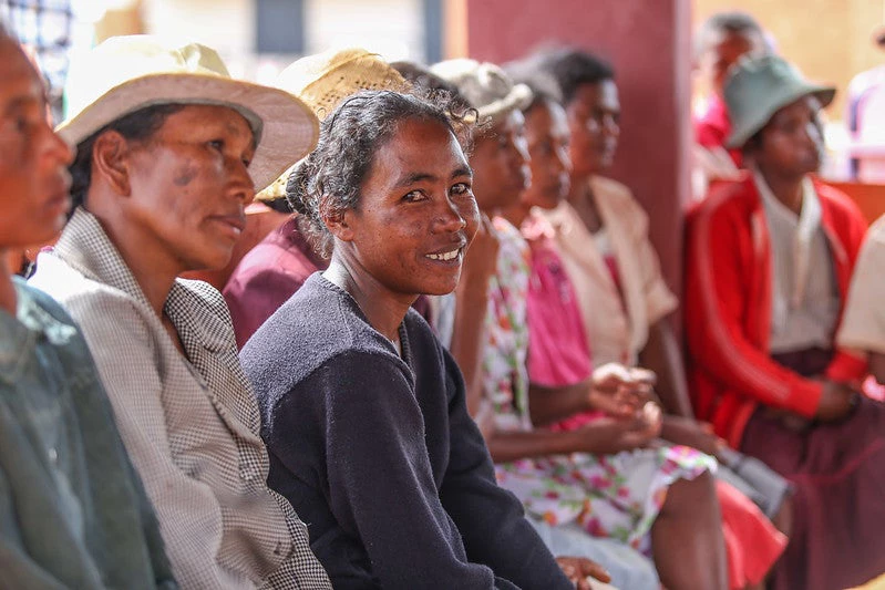 Women sitting in a row of chairs and looking forward, one women is looking into the camera and smiling