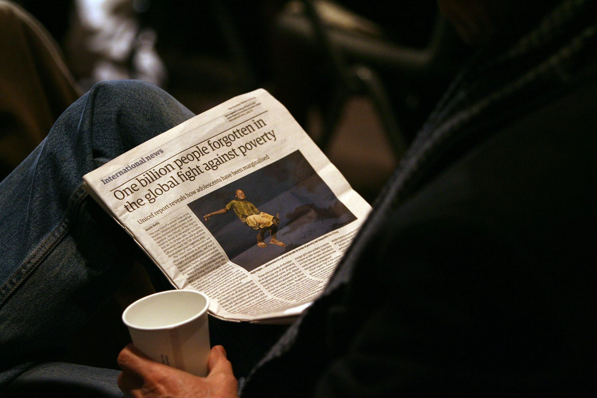 Persona leyendo prensa. Titular dice: "Mil millones de personas olvidadas en la lucha mundial contra la pobreza."