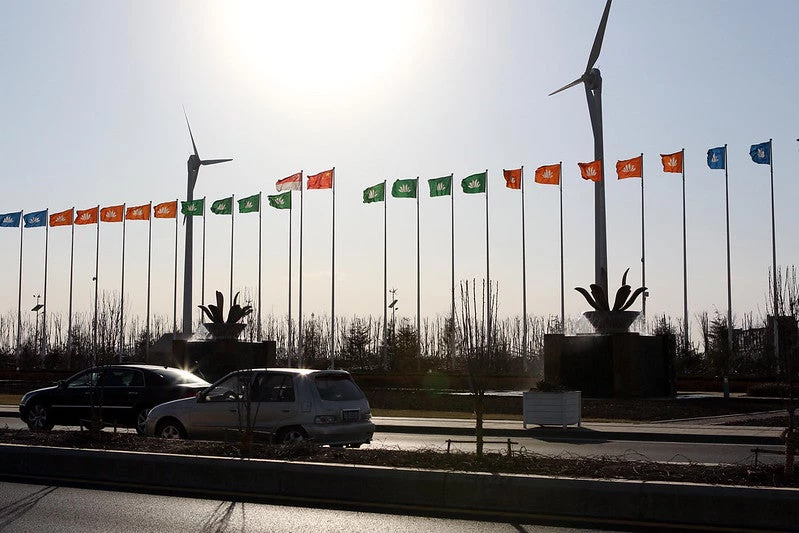 Two windmills in front of a long row of small flags, behind a street