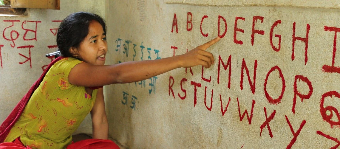 A teach in rural Nepal points to letters as she teaches her class how to read the English