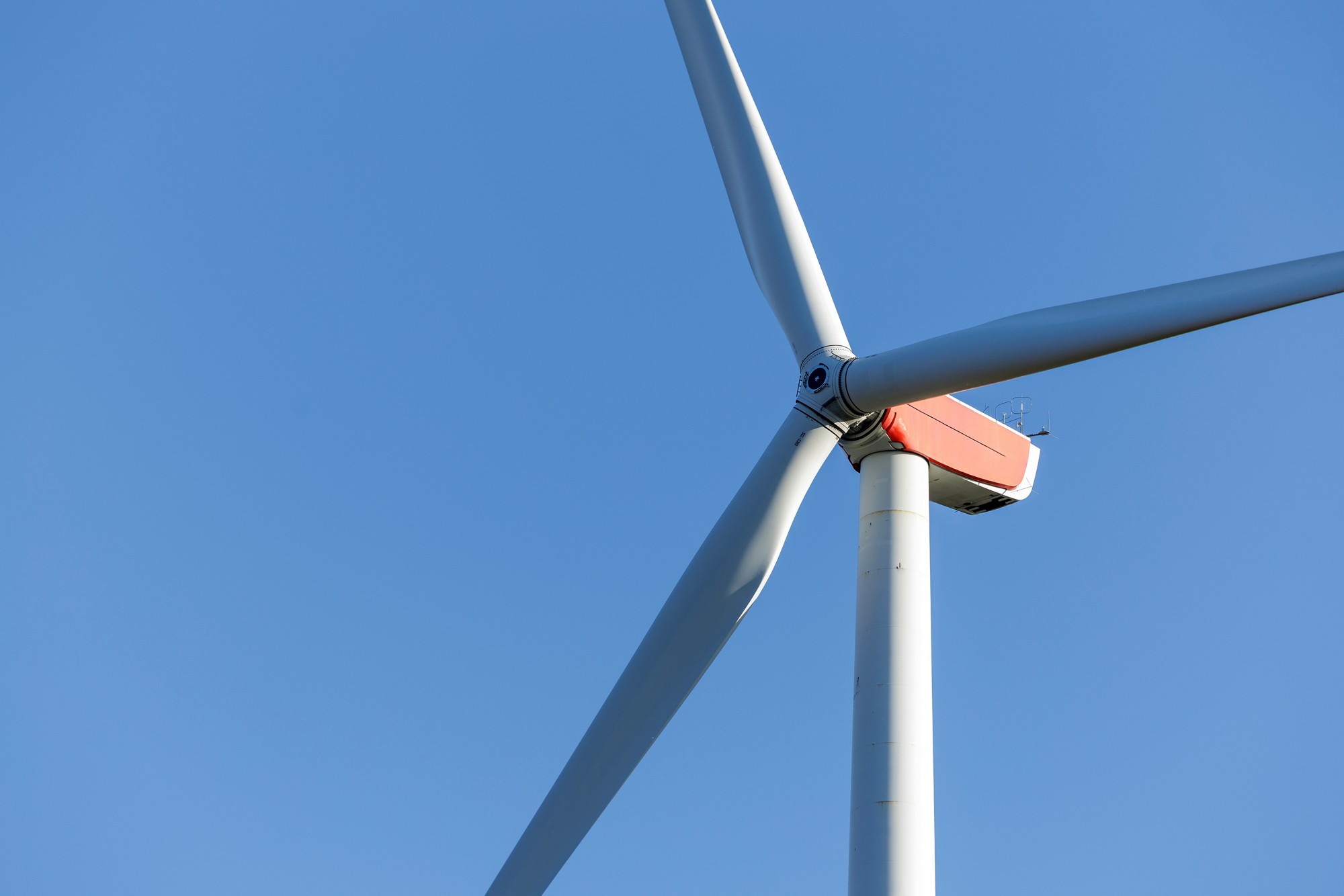 all wind turbines rise over open farmland beneath a clear blue sky. Captured in natural daylight, the scene highlights renewable energy, sustainability, and harmony between technology and nature.