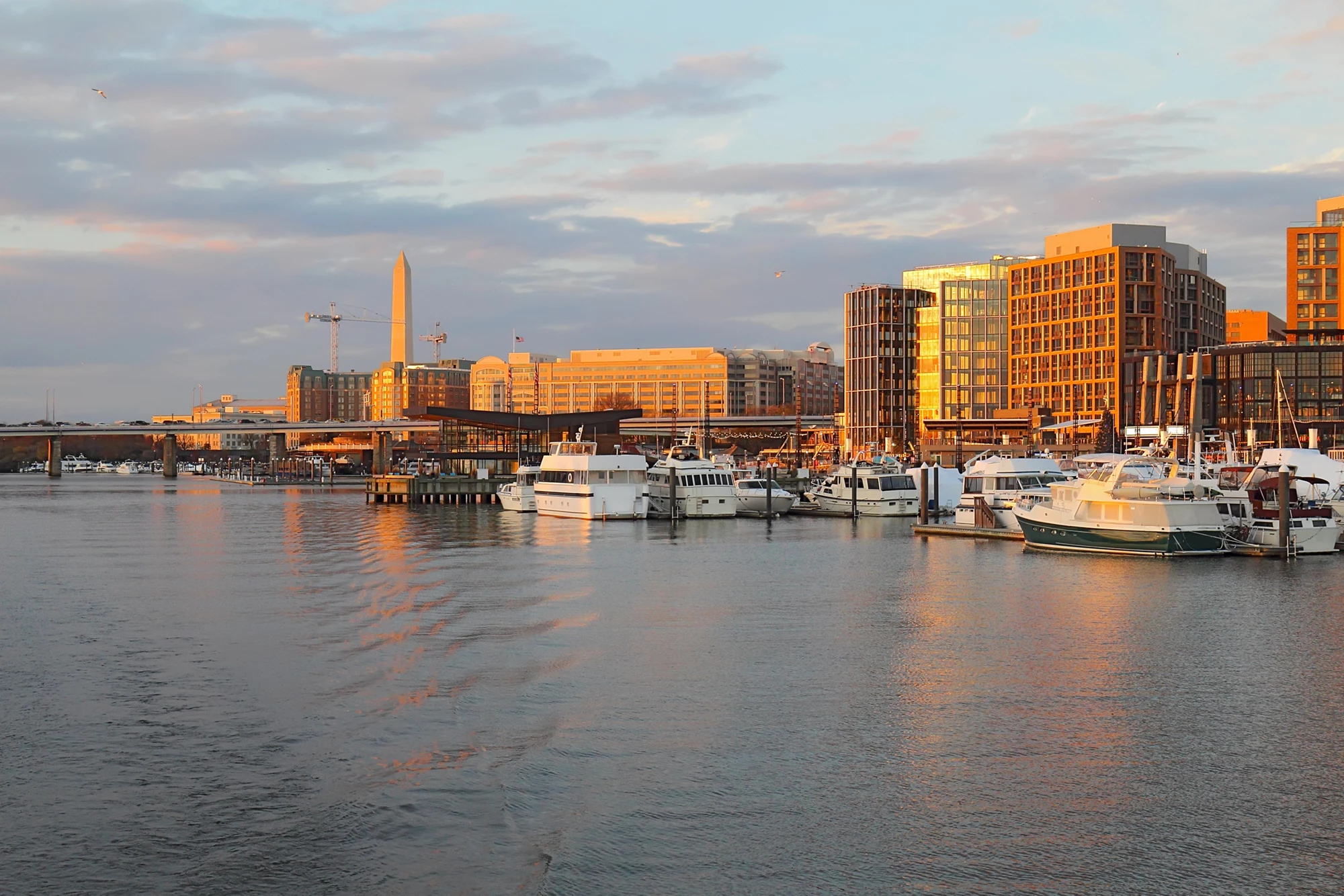 The Wharf, boats and skyline of buildings at the newly redeveloped Southwest Waterfront area of Washington, DC viewed from the water at sunset in fall with the Washington Monument in the background