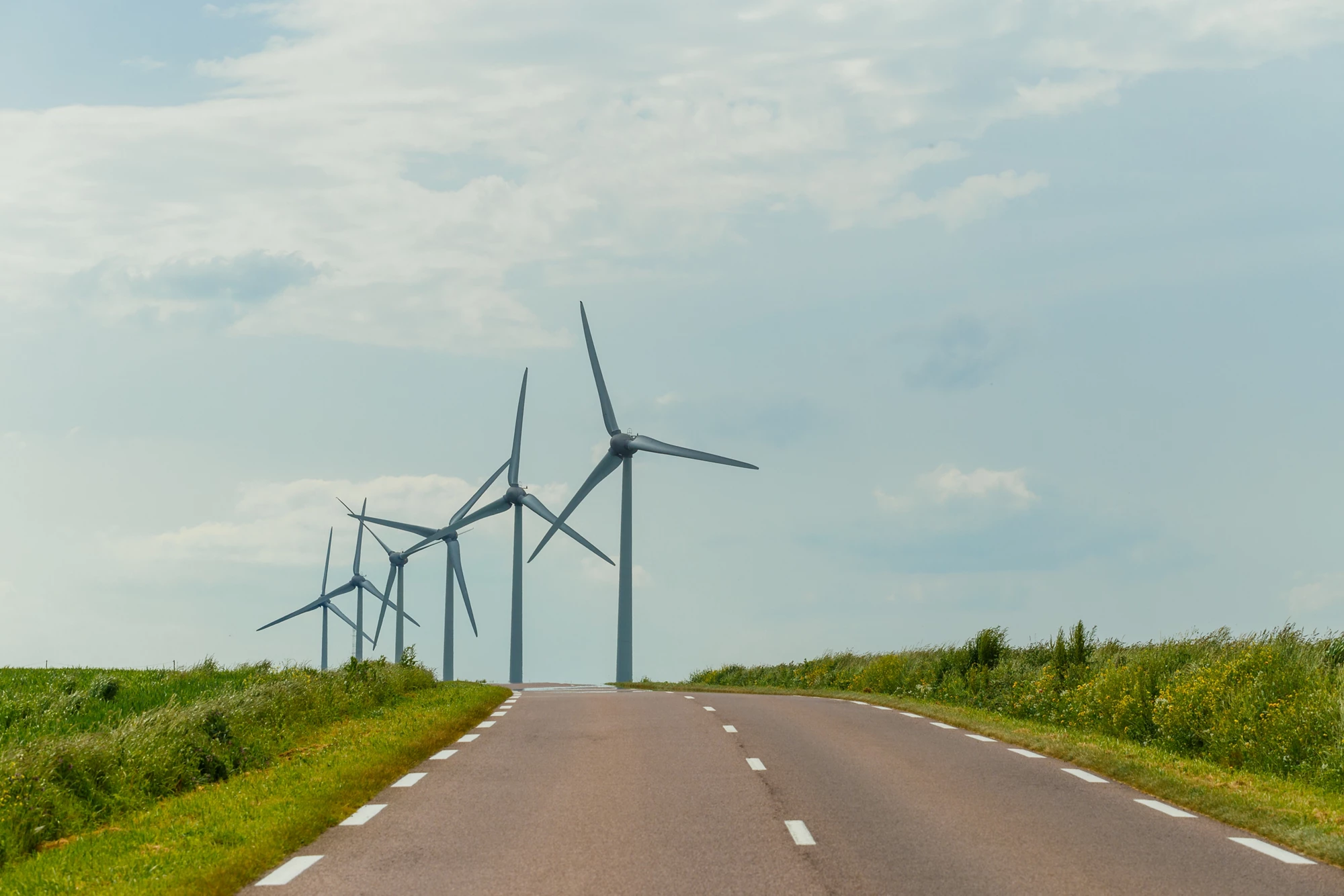 Wind turbines of a power plant for electricity generation close to country road in Normandy, France. Countryside landscape. Environmentally friendly electricity production.